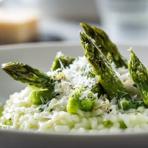 Cremiges Spargelrisotto aus dem Ofen mit grünem Spargel und frisch geriebenem Parmesan, serviert auf weißem Teller