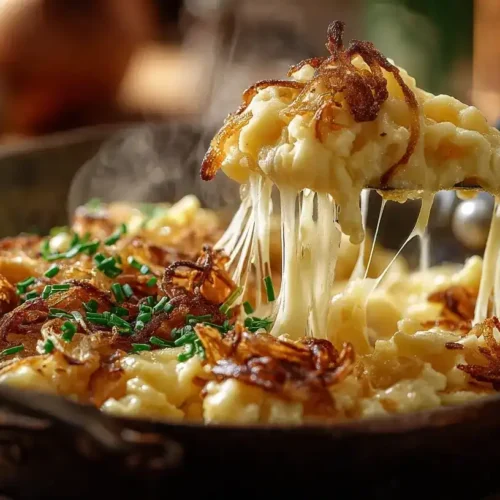 Käsespätzle mit Röstzwiebeln in einer gusseisernen Pfanne, cremig mit geschmolzenem Bergkäse und frischem Schnittlauch
