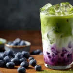 Servierter Iced-Blaubeer-Matcha-Latte mit Eiswürfeln und frischen Blaubeeren